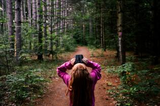 a young girl standing on a forest path looks up at the tree canopy through binoculars